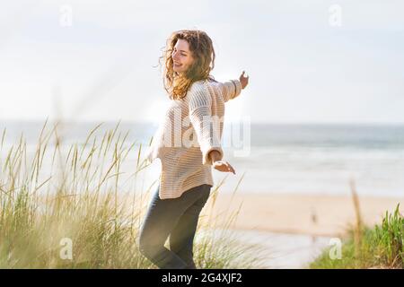 Carefree woman with arms outstretched standing amidst dunes at beach Stock Photo