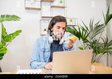 Businessman talking on smart phone though speaker while using laptop in office Stock Photo