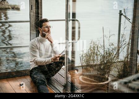 Thoughtful male professional wearing eyeglasses working on houseboat Stock Photo