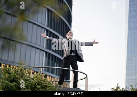 Ecstatic businessman with arms outstretched standing in front of office building Stock Photo