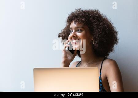 Smiling university student with laptop talking on mobile phone Stock Photo