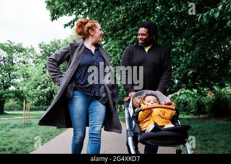 Father talking to mother while walking wheeling son in stroller at park Stock Photo