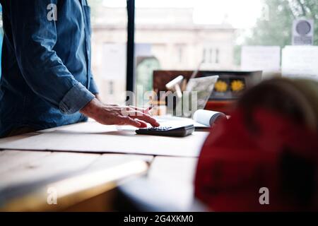 Male store owner using calculator while making financial bill in workshop Stock Photo