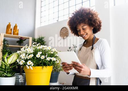Female shop owner using digital tablet while standing at plant shop Stock Photo