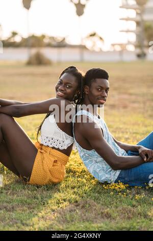 Smiling couple leaning while sitting back to back at grass area Stock Photo