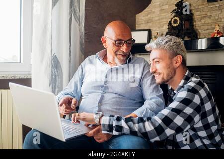 Smiling father and son sharing laptop while sitting together at home Stock Photo