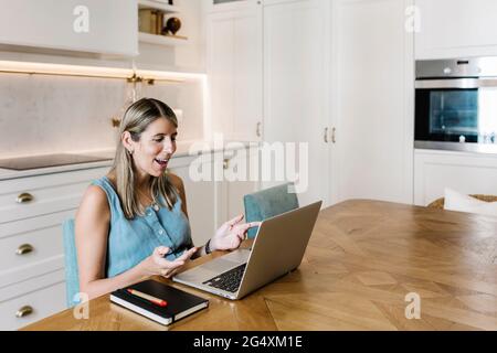 Businesswoman gesturing during video conference through laptop in kitchen at home Stock Photo