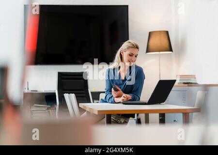 Female entrepreneur using laptop sitting at desk in office Stock Photo