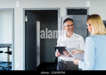 Smiling male entrepreneur looking at female professional reading document while discussing in office Stock Photo