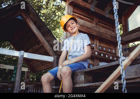 Smiling boy wearing yellow hardhat in rabbit hutch Stock Photo