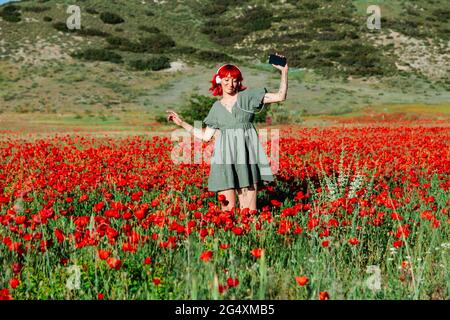 Young woman with smart phone dancing on poppy field during sunny day
