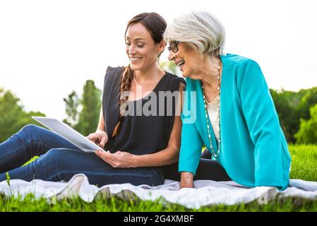 Smiling women using digital tablet while sitting on picnic blanket Stock Photo