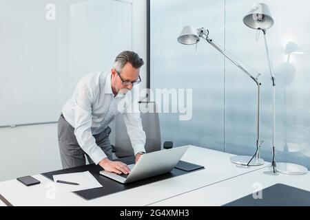 Young male entrepreneur working on laptop while standing at desk Stock Photo