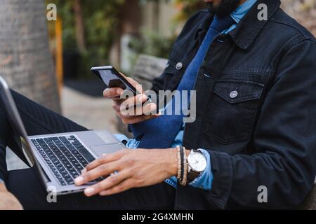 Male entrepreneur with laptop using mobile phone Stock Photo