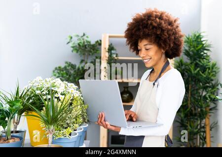 Smiling florist using laptop while standing by plants in shop Stock Photo