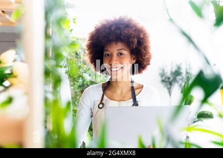 Female shop owner with laptop smiling at plant store Stock Photo
