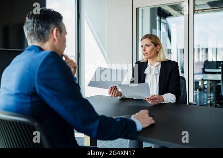 Businesswoman holding documents while discussing with colleague during meeting in board room Stock Photo