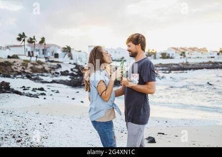 Couple toasting beer bottles while standing at beach Stock Photo