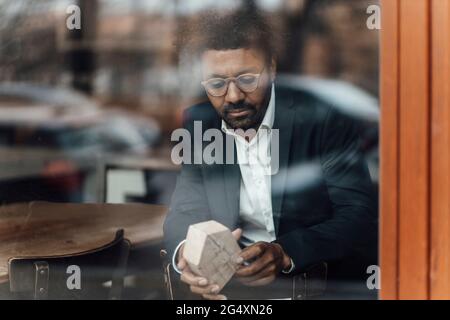 Mature businessman with house model sitting in cafe seen through glass Stock Photo