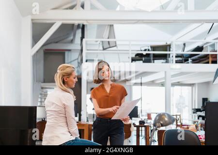 Female colleagues discussing over document in creative office Stock Photo