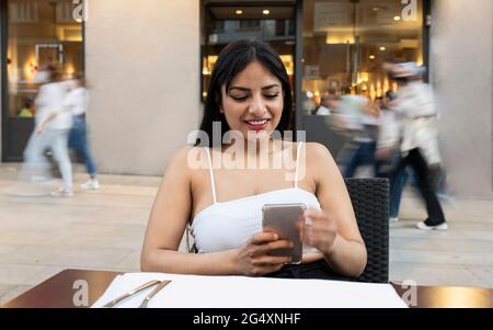 Smiling young woman using mobile phone at sidewalk cafe Stock Photo