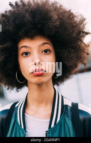 Young mixed woman with afro hair standing on the street. Female wearing ...