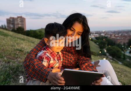 Smiling mother and son using digital tablet while sitting on hill Stock Photo
