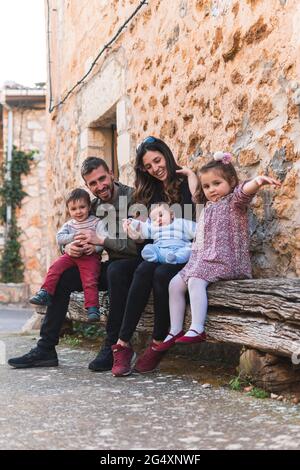 Happy family sitting on bench with house in background Stock Photo