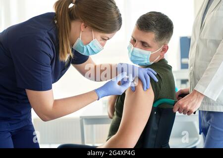 Female doctor giving COVID-19 vaccine to disabled man sitting on wheelchair at vaccination center Stock Photo
