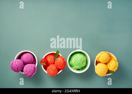 Gourmet flavours of Italian ice cream in vibrant colors served in individual ice cream paper cups on blue background. Strawberry sorbet, blueberry or Stock Photo