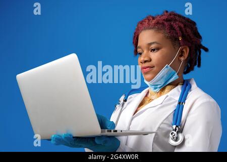 Young african american woman doctor using laptop against blue background Stock Photo
