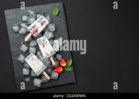 Refreshing, healthy ice cream with chia seeds and fresh strawberries on ice cubes on a black background. Stock Photo