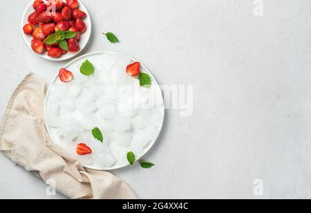 A plate of ice cubes and strawberries with mint on a gray background Stock Photo