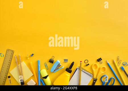 Row of yellow and blue school supplies on yellow background and top empty space. Top view. Horizontal composition. Stock Photo