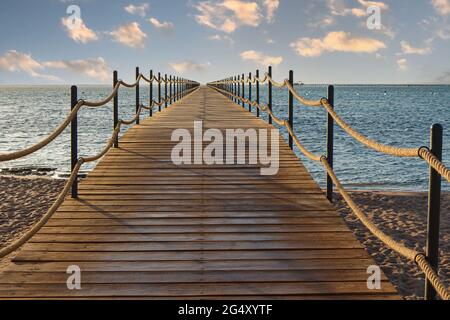 Wooden pier extending into the sea at sunrise Stock Photo