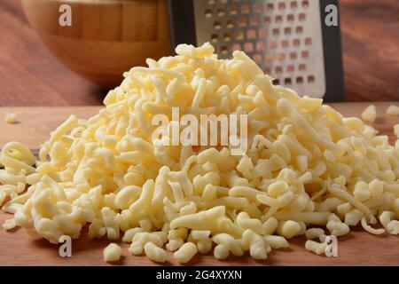 Heap of shredded cheese on small wooden board. Grated cheese for cooking on a cutting board on a wooden background Stock Photo