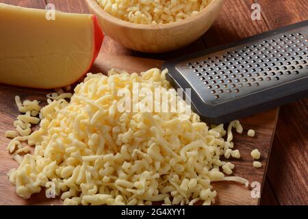 Heap of shredded cheese on small wooden board. Grated cheese for cooking on a cutting board on a wooden background Stock Photo