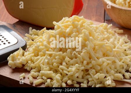 Heap of shredded cheese on small wooden board. Grated cheese for cooking on a cutting board on a wooden background Stock Photo