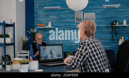 Young doctor video conferencing senior woman,remote patient consulting about corona virus pandemic during telemedicine video call in conference virtual webcam chat app. Over shoulder laptop screen view Stock Photo