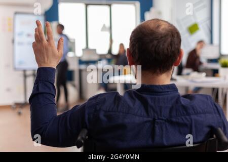 Independence handicapped businessman entrepreneur coming in start up office waving sitting immobilized in wheelchair greetting business team, diverse colleagues welcoming in startup financial company. Stock Photo