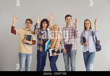 Students vote or are ready to answer questions standing with raised hands on a gray background. Stock Photo