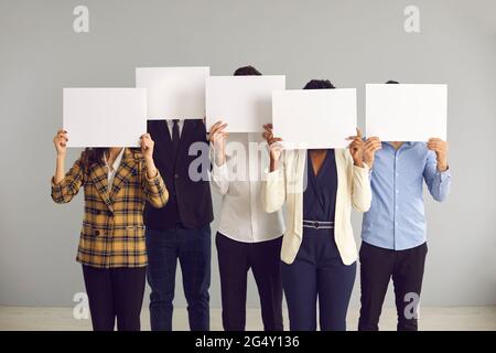 Group of anonymous people covering faces hiding behind white mockup sheets of paper Stock Photo
