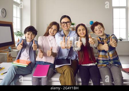 Happy teacher and smiling elementary school students holding thumbs up Stock Photo