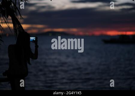 A girl is taking a photo of sunset over the sea Stock Photo
