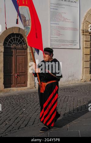 This standard bearer wearing splendid medieval clerical costume recalls the illustrious past of Anagni, Lazio, Italy, as City of the Popes, the summer retreat between the 11th and 14th centuries of pontiffs who preferred its relative cool to the sweltering heat of Rome.  Anagni was also the birthplace of popes Gregory IX and Boniface VIII.  The standard for Anagni’s Cellere Contrada (traditional district) is being carried in a procession honouring 3rd century AD bishop and martyr San Magno di Anagni (Saint Magnus of Anagni), the town’s patron saint. Stock Photo