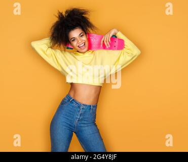 Cheerful girl with longboard on yellow background Stock Photo