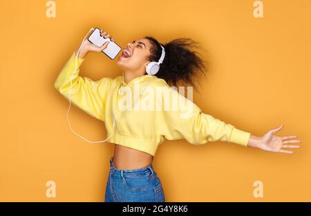 Cheerful girl listens favorite song in headphones, sings words on yellow background Stock Photo