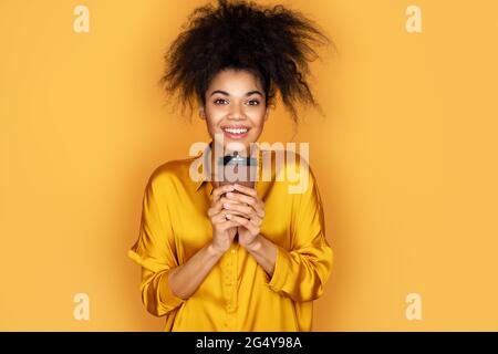 Young girl holds paper cup with hot coffee, takeaway. Photo of african american girl on yellow background Stock Photo