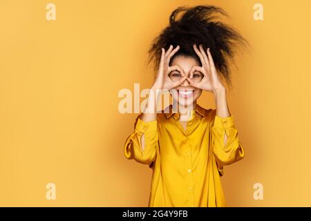 Smiling girl shows ok sign with both hands, says good job or well done. Photo of african american girl on yellow background Stock Photo