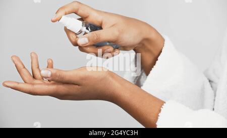 Cropped view of african american woman in bathrobe using hand sanitizer isolated on grey
